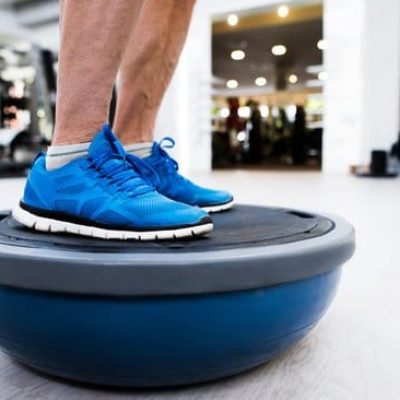 Close up of legs of senior man in gym standing on bosu balance ball and exercising as part of bodybuilding training